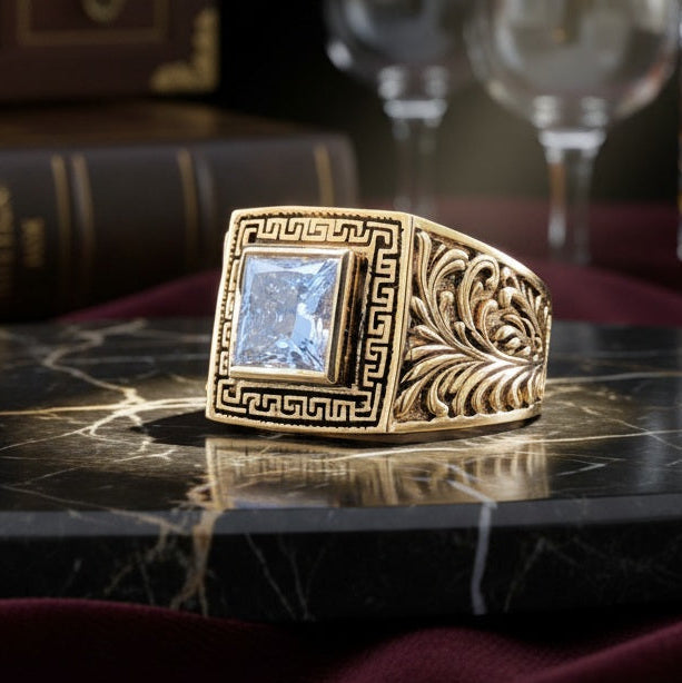 Decorative ring with a prominent gemstone on a dark surface, with books and glasses in the background.