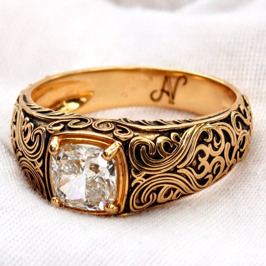 Gold ring with intricate design and diamond on a white fabric background